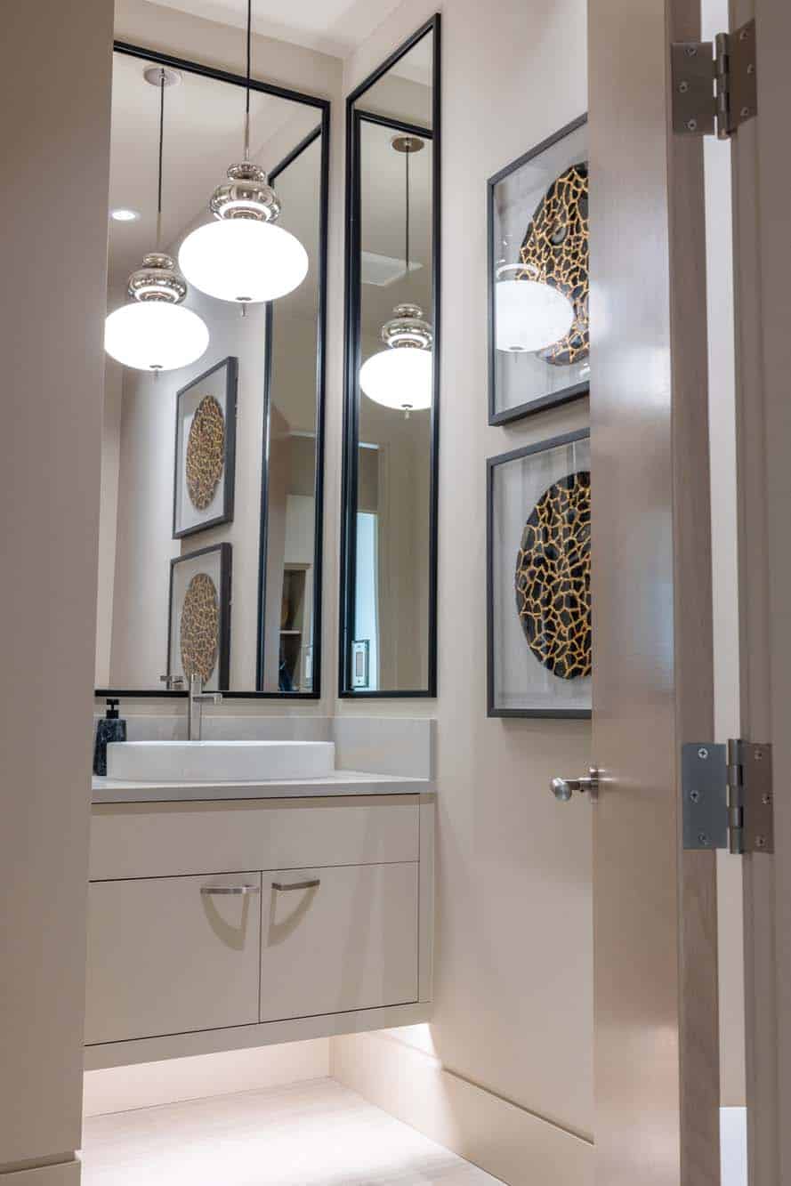 Modern bathroom with a floating vanity, vessel sink, two hanging pendant lights, two tall mirrors, and framed abstract wall art—expertly enhanced by custom finish carpentry in Bellevue. The door is partially open.