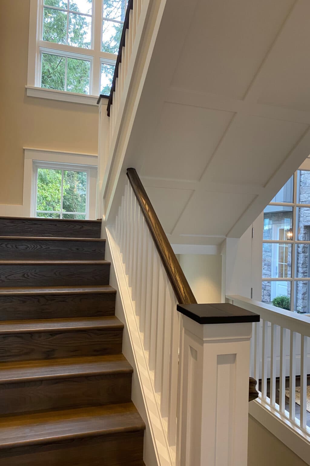 Interior view of a staircase with dark wooden steps, white railings, and large windows letting in natural light, showcasing the elegance and attention to detail achieved through custom finish carpentry Medina.